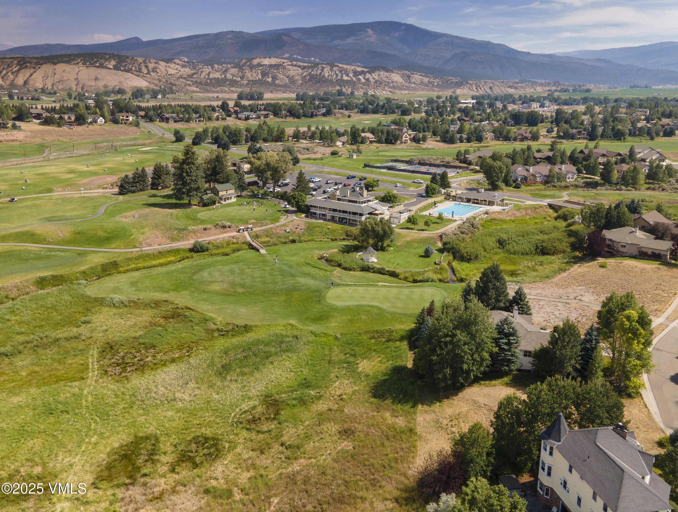 Aerial view of a golf course community with a pool and clubhouse beneath the mountains.