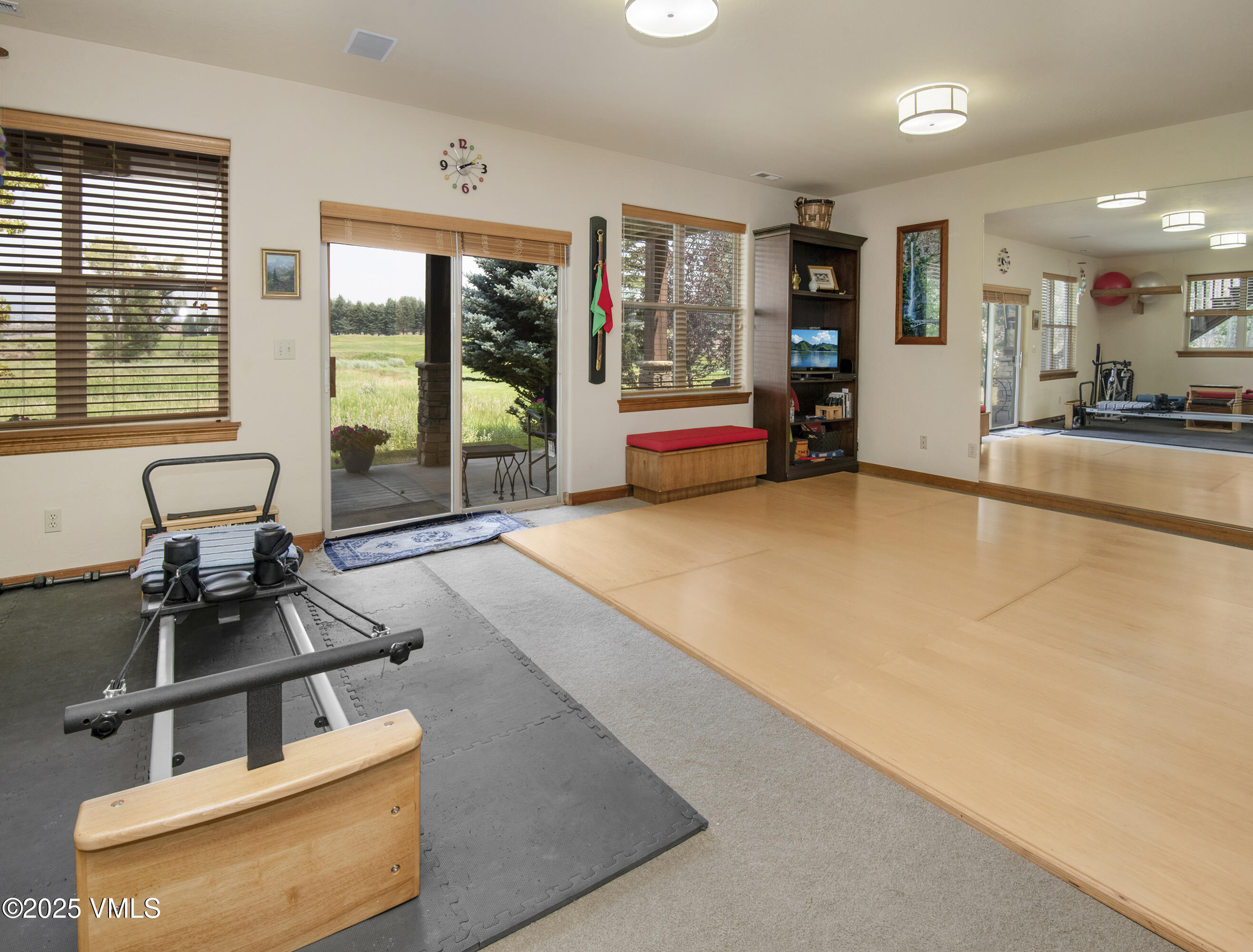 Exercise room with a Pilates reformer, broad wood floor, and sliding glass door to a grassy landscape.