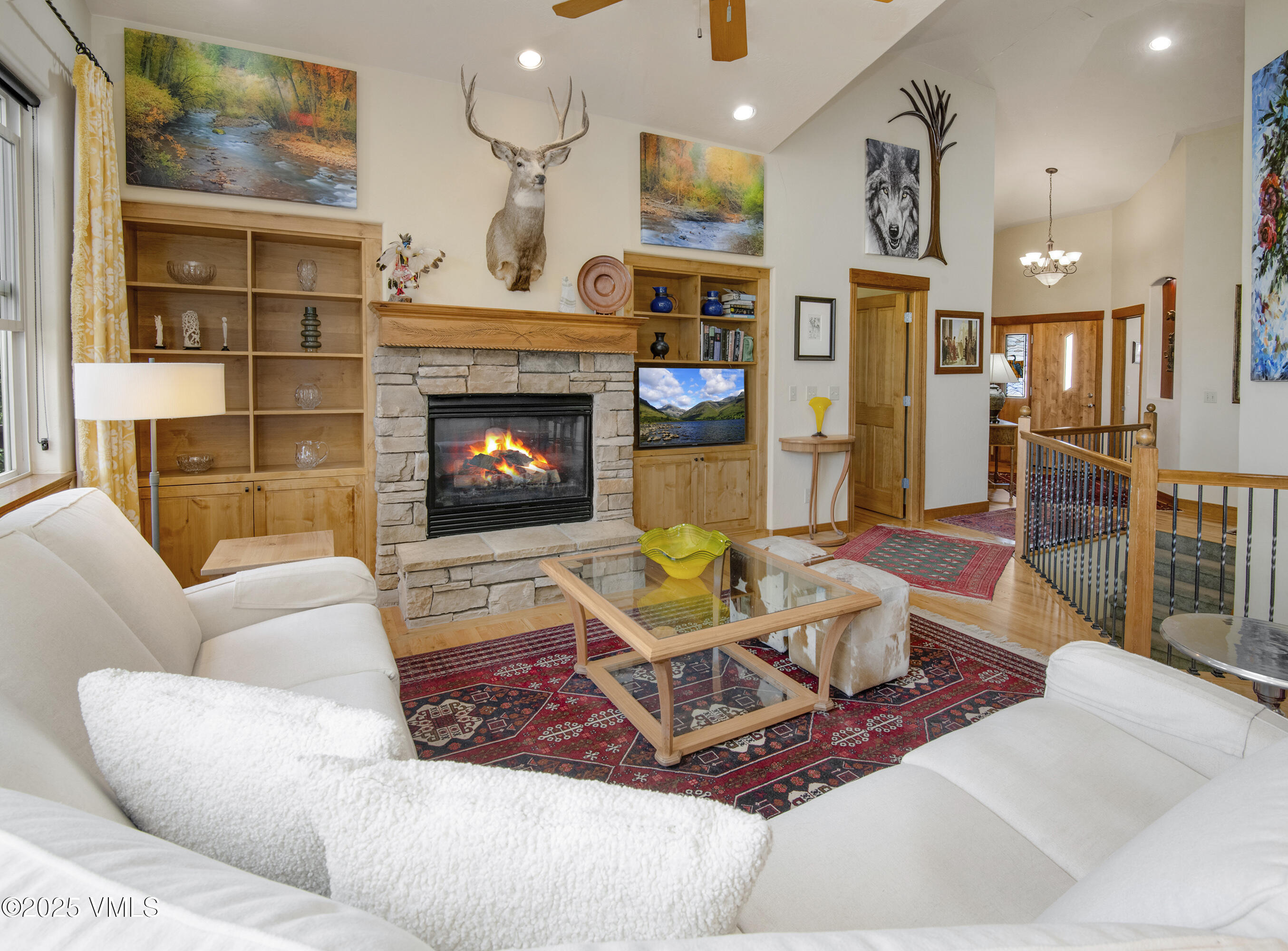 Living room with a stone fireplace, wood built-ins, white sofas, and a mounted deer head.