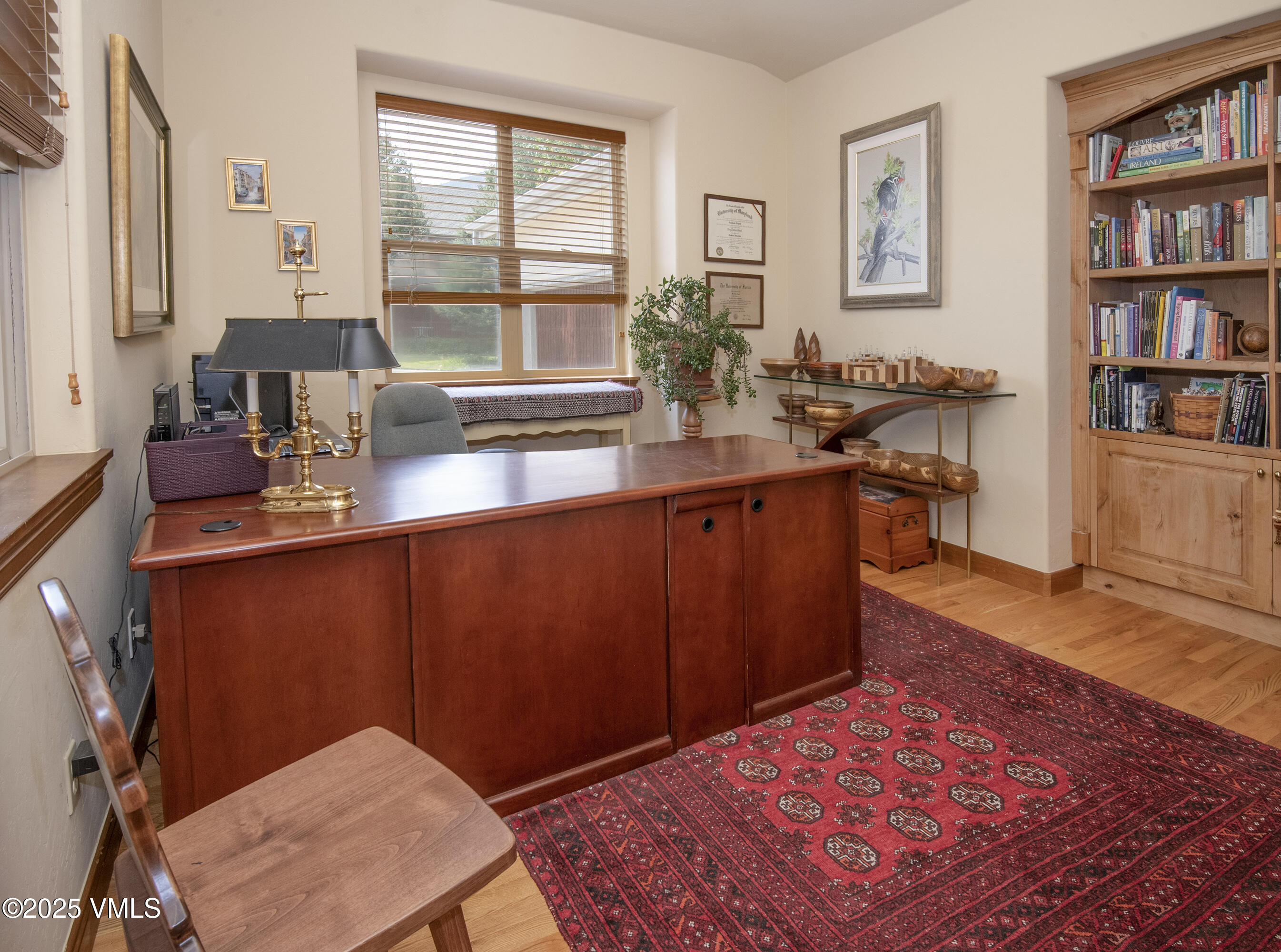 Furnished home office with a large wood desk, built-in bookcase, and patterned red rug.