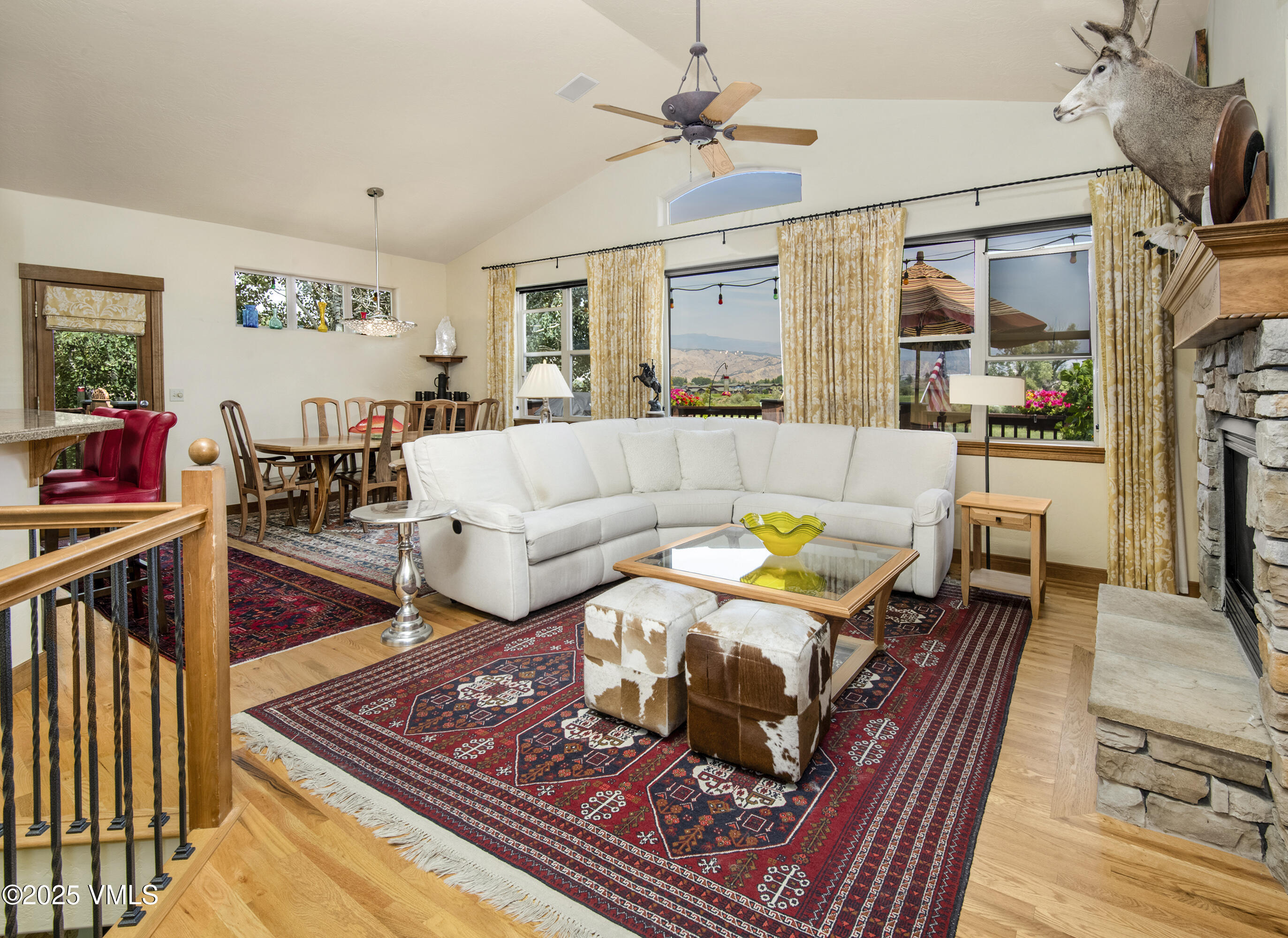 Living room with a white sectional, stone fireplace, patterned rugs, and mountain views through large windows.