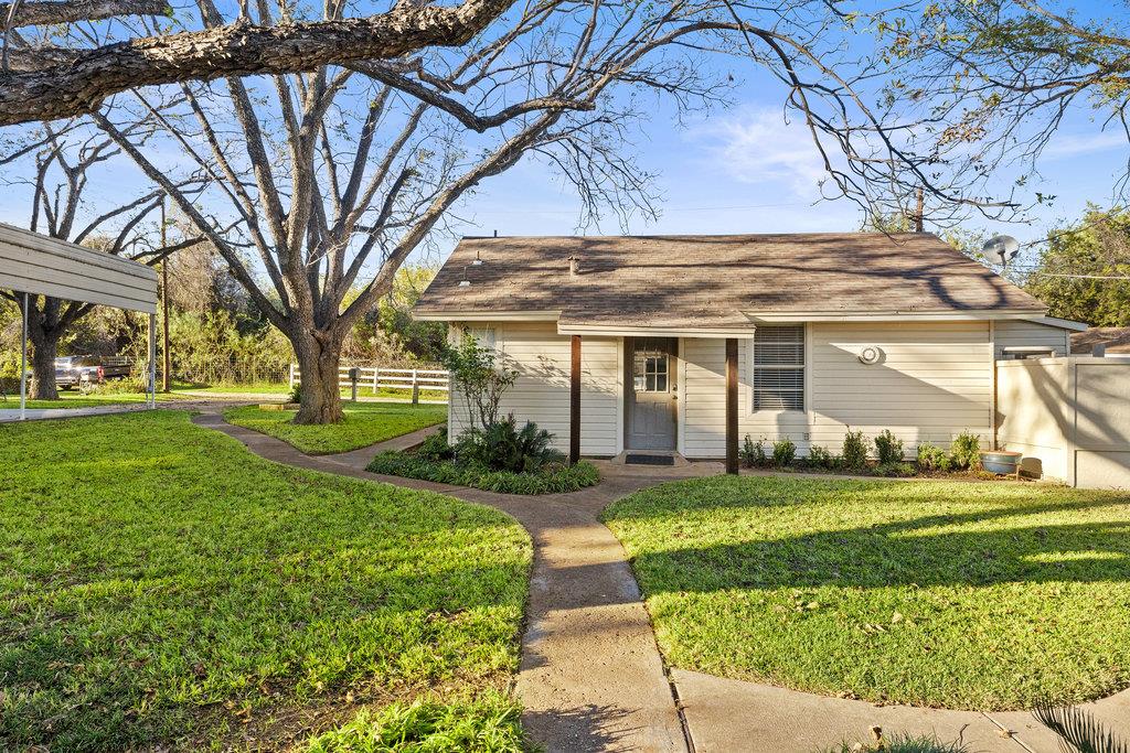 Single-story house with a covered entry, curving walkway, and large shade tree in the yard.
