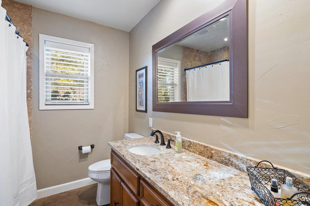 Bathroom with a granite vanity, large framed mirror, and window with white blinds.