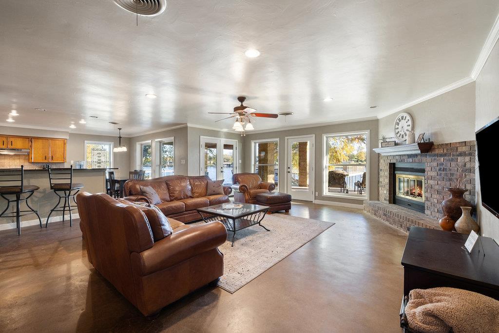 Living room with brown leather seating and a brick fireplace beside large windows and glass doors.