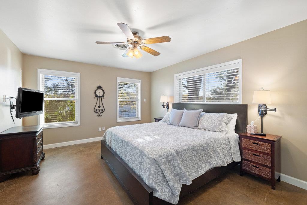 Bedroom with a king-size bed, three windows with blinds, and a ceiling fan.