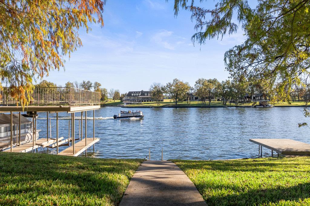 Lakefront view with a concrete path, covered dock, and boat crossing the water.