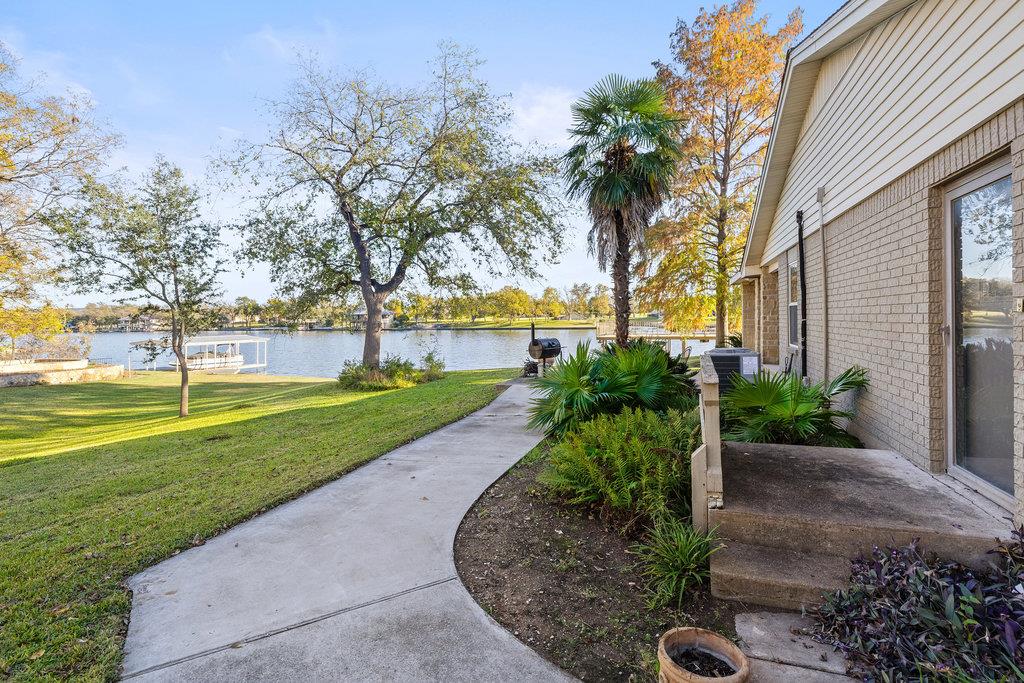Lakeside home exterior with a curved walkway, landscaped yard, and dock across the water.
