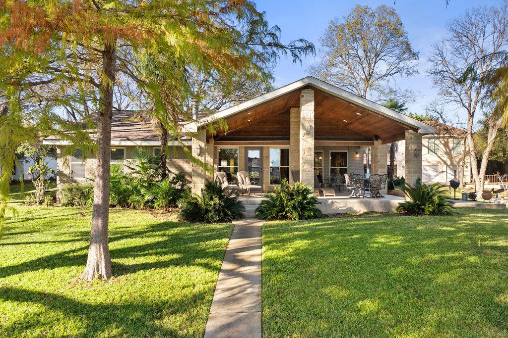 Home’s rear exterior with a broad covered patio, stone columns, outdoor seating, and a lawn-side walkway.