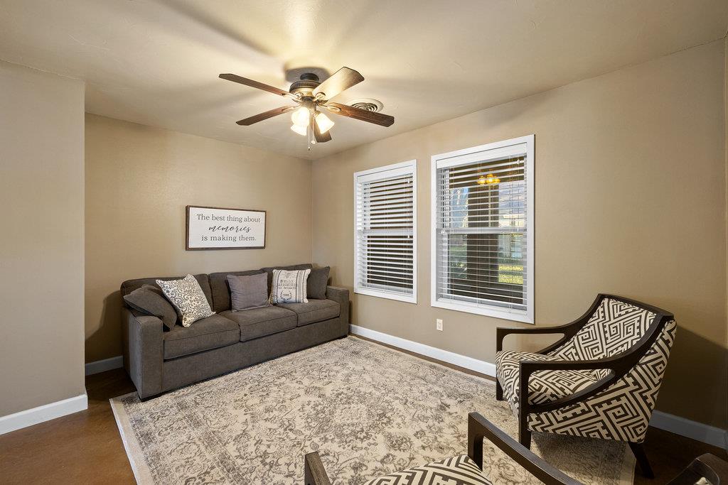 Living room with a gray sofa, patterned armchair, two windows, and a ceiling fan with lights.