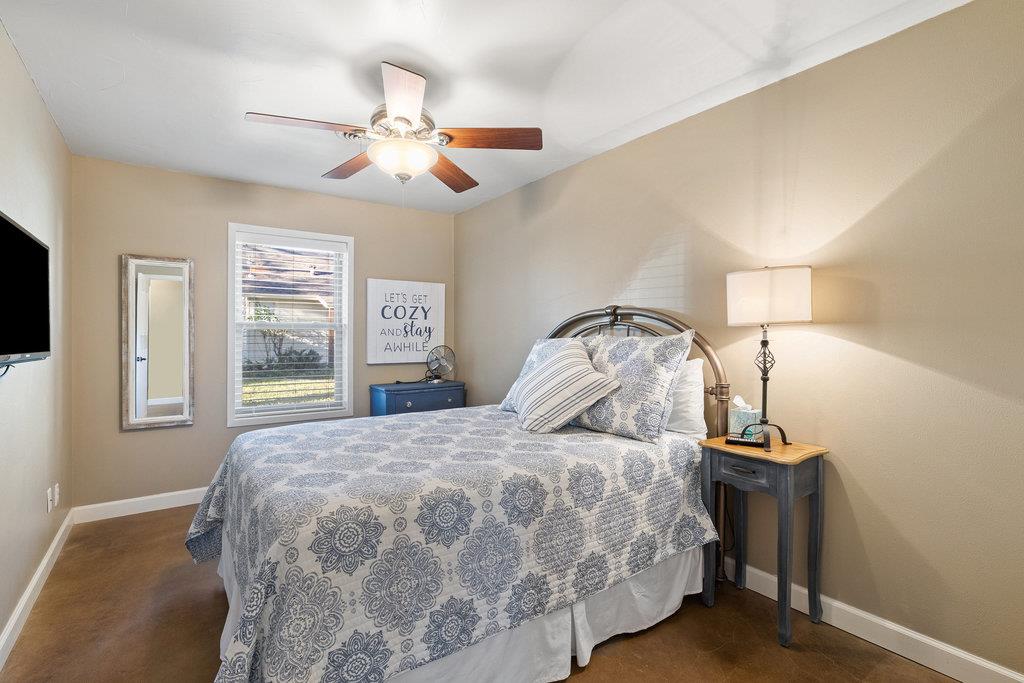 Bedroom with a patterned bedspread, ceiling fan, window, and bedside lamps.