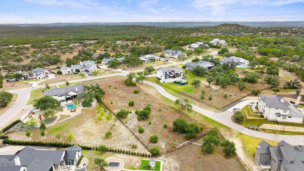 Aerial view of homes and open lots along winding streets, with wooded countryside beyond.