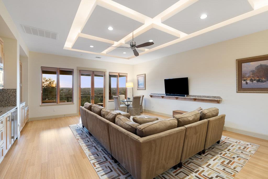 Living room with a coffered ceiling, large sectional sofa, and tall windows overlooking trees.