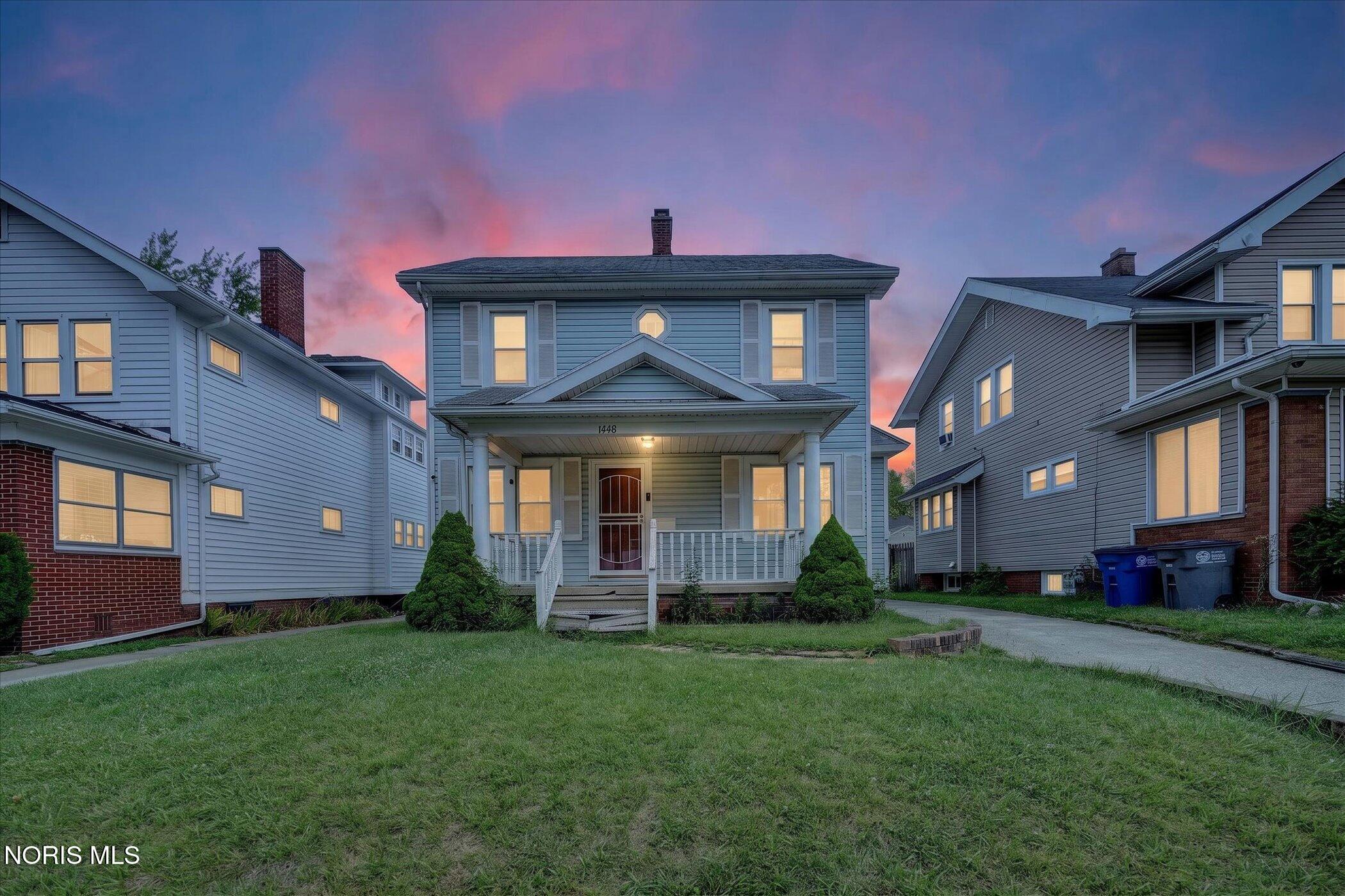 Two-story blue-gray house with a covered porch and illuminated windows at dusk.