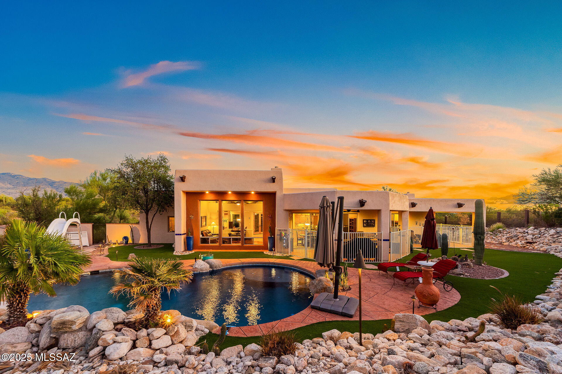Modern Southwestern home with a curved pool and desert landscaping at sunset.