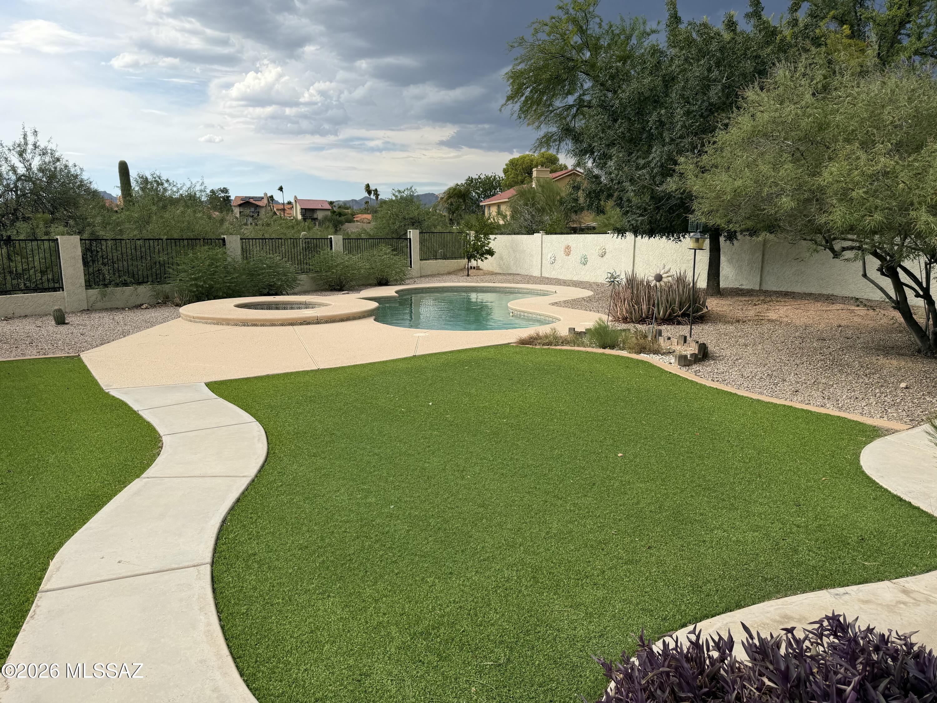 Backyard pool and raised spa beside a curved walkway, green lawn, and desert landscaping.