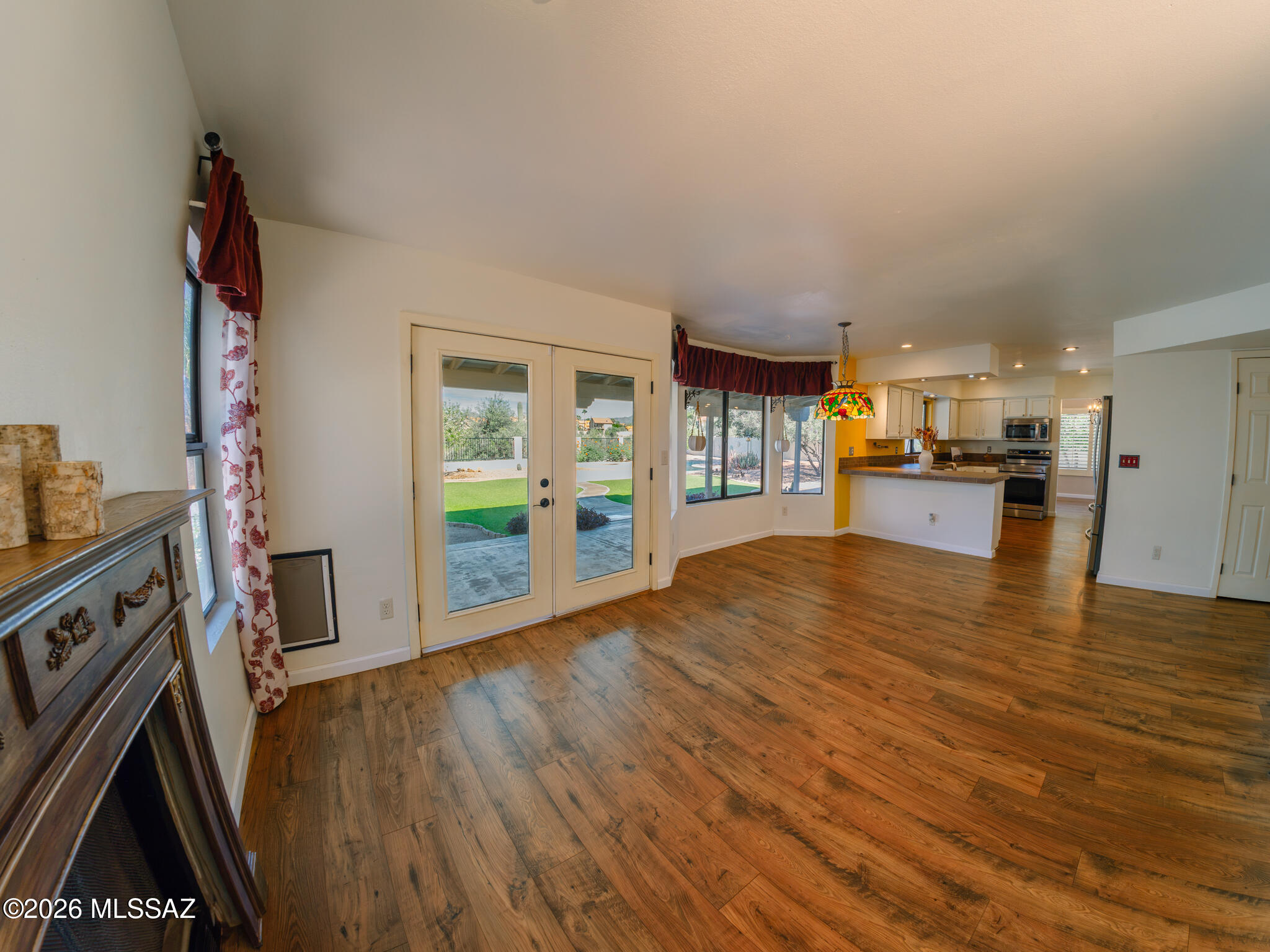 Open-plan living and dining area with wood-look floors, French doors to the patio, fireplace, and kitchen island.