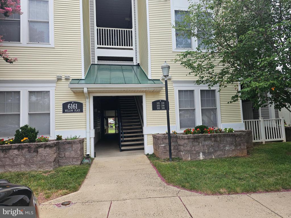 Residential building entrance at 6161 Willow Place, with a covered entry, exterior staircase, and flower beds.