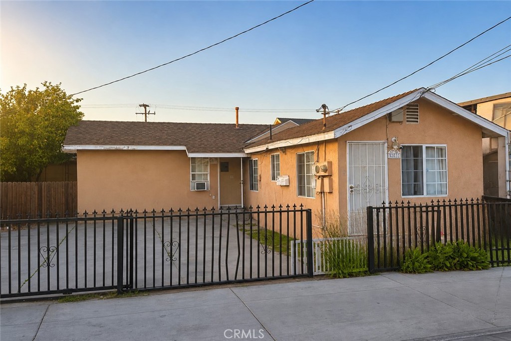Single-story tan home with a black metal fence and gated concrete driveway.