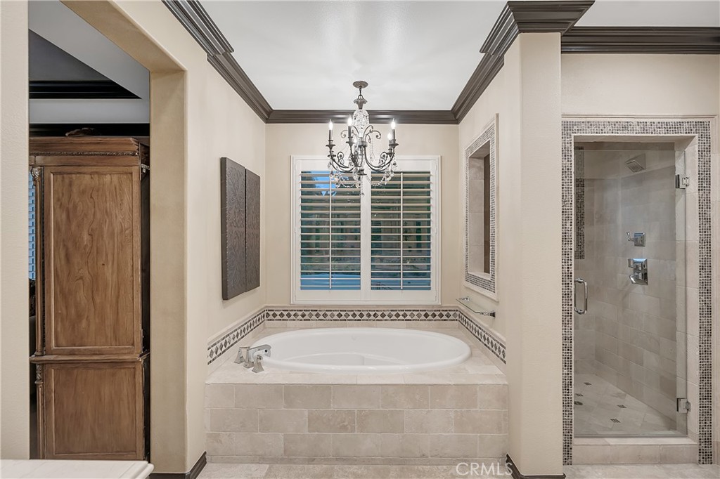 Primary bathroom with an oval soaking tub, shuttered window, chandelier, and glass-enclosed tiled shower.