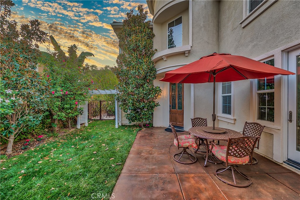 Backyard patio with a red umbrella over a dining set beside a lawn and garden arbor.