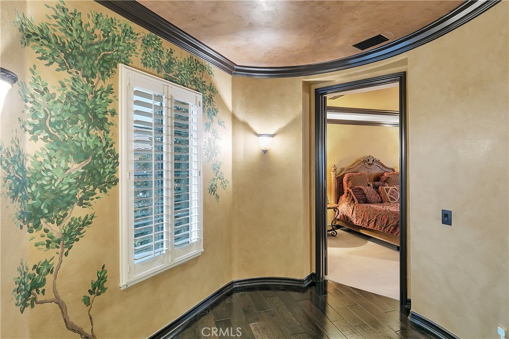 Hallway with a leafy tree mural and shuttered window, looking into a furnished bedroom.