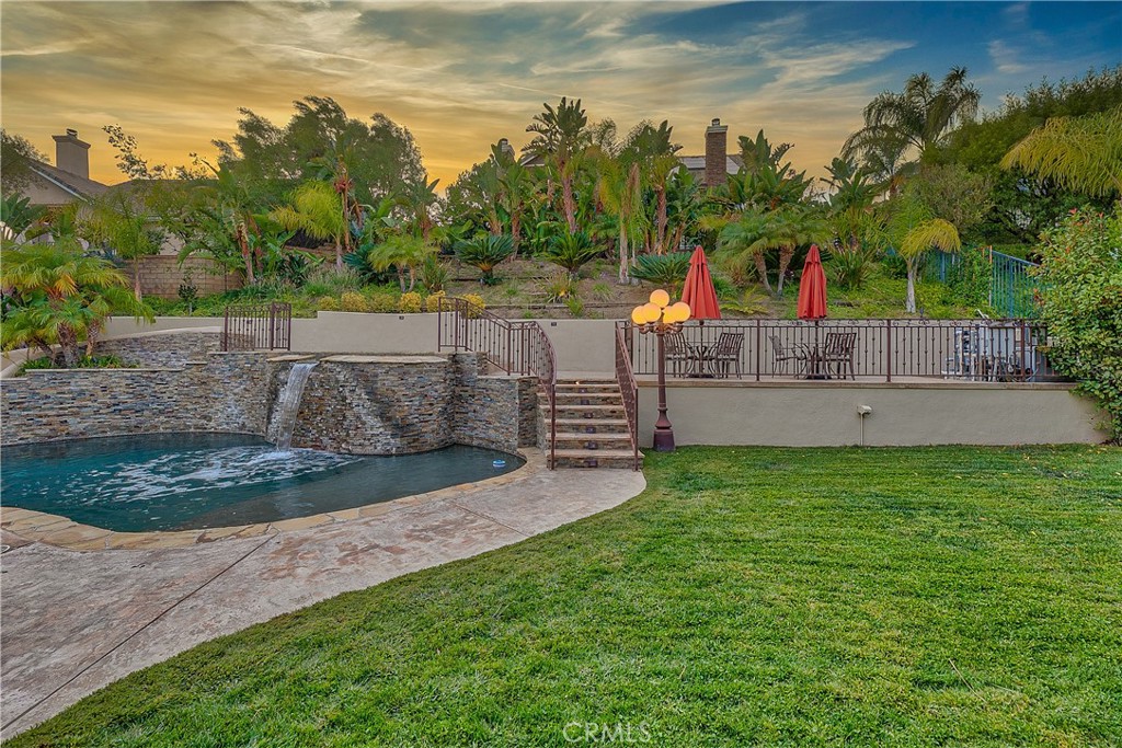 Backyard pool and spa with a stone waterfall, raised dining patio, and tropical landscaping.