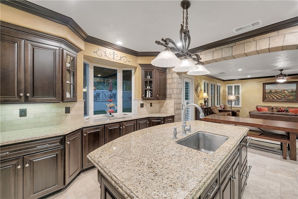 Kitchen with dark wood cabinets, a large stone island, and a sink, opening to the living area.