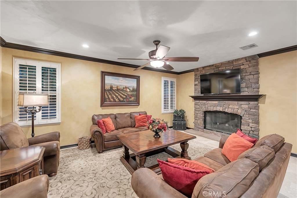Living room with leather seating, plantation shutters, and a stone fireplace beneath a mounted television.