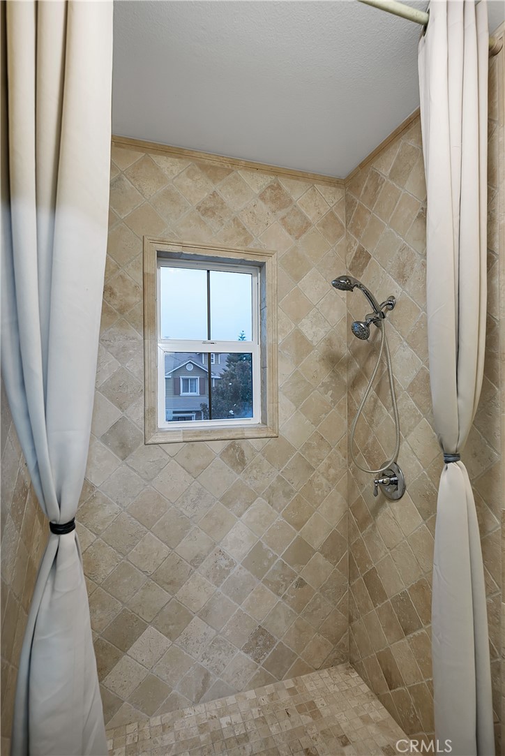 Walk-in shower with beige stone tile, a small window, and a handheld showerhead.