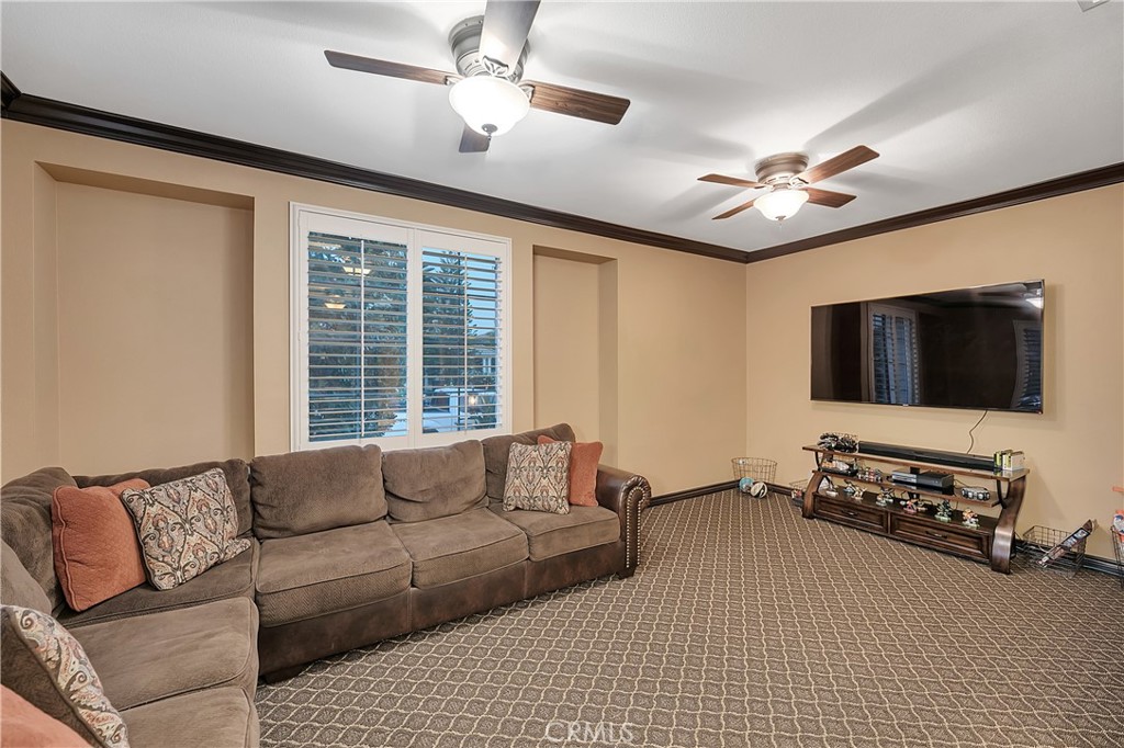 Living room with a brown sectional, shuttered window, two ceiling fans, and wall-mounted television.