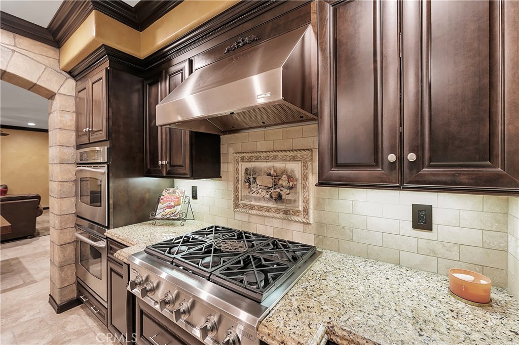 Kitchen with a stainless steel range, dark wood cabinets, granite counters, and a decorative tiled backsplash.
