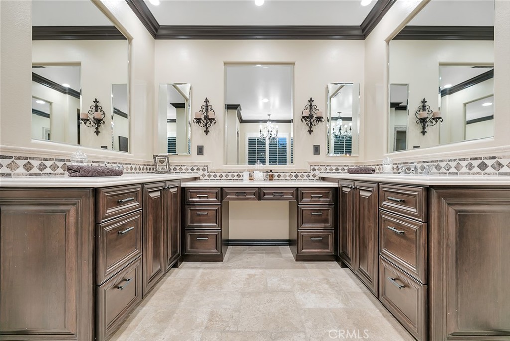 Bathroom vanity with dark wood cabinetry, mirrored walls, and a decorative tile backsplash.