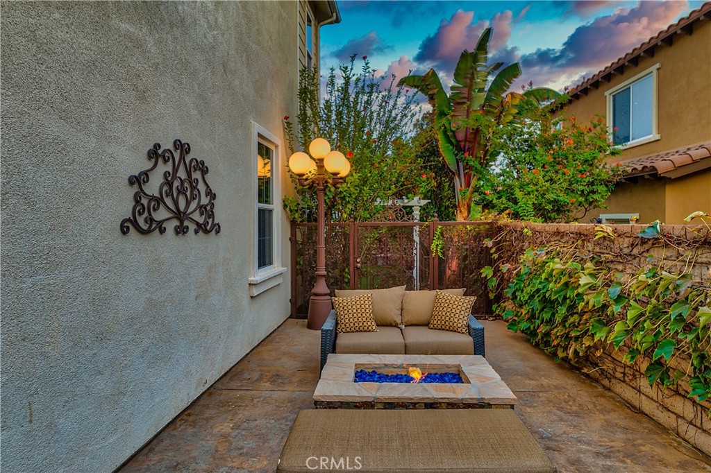 Enclosed courtyard patio with a sofa, rectangular fire pit, tropical plants, and a glowing three-globe lamp.
