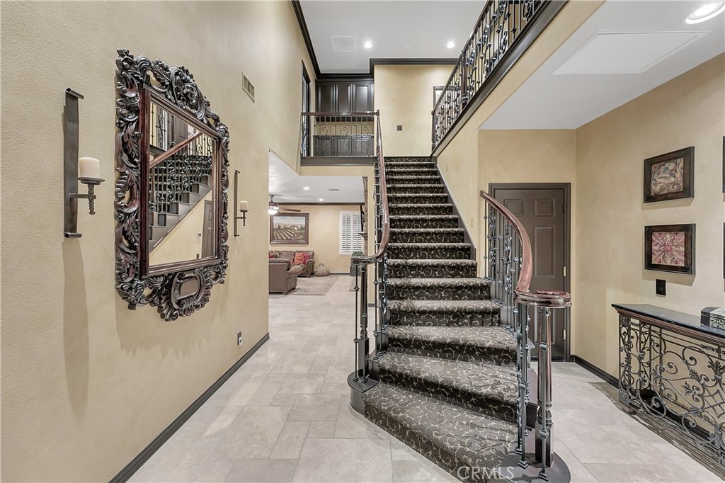 Two-story foyer with a curved carpeted staircase, ornate metal railings, and a large carved mirror.
