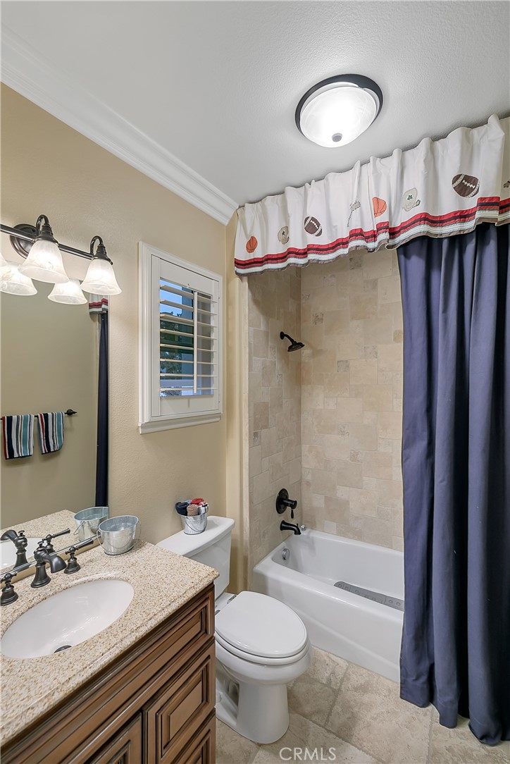 Bathroom with a granite vanity, beige tiled tub and shower, and sports-themed curtain valance.