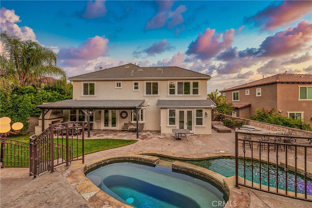 Two-story home with a covered patio and pool with an attached spa at dusk.