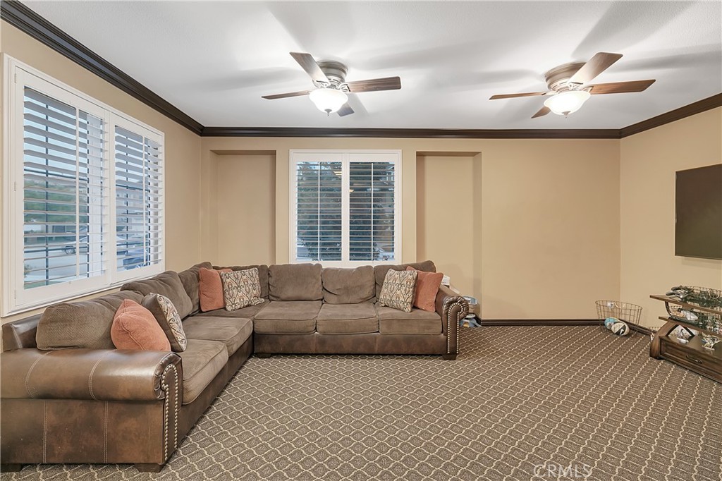 Living room with a brown sectional, patterned carpet, two ceiling fans, and shuttered windows.
