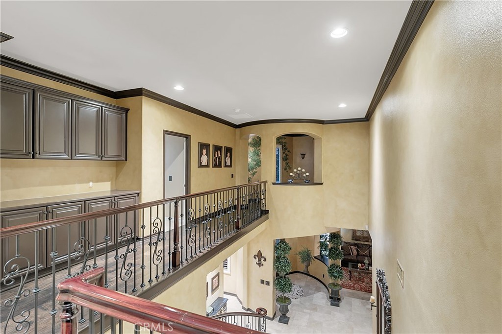 Upper landing overlooking a two-story foyer, with dark built-in cabinets and a decorative iron railing.