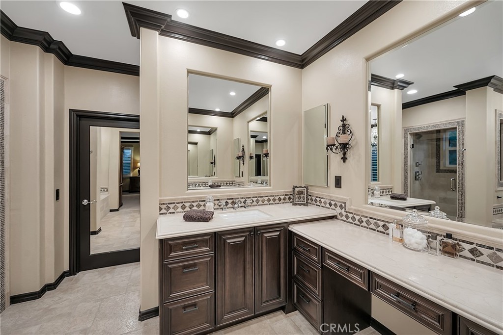 Bathroom with an L-shaped stone vanity, dark wood cabinets, decorative tile, and a glass-enclosed shower.