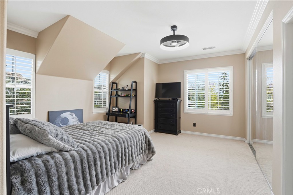 Bedroom with a gray textured bedspread, shuttered windows, and mirrored closet doors.