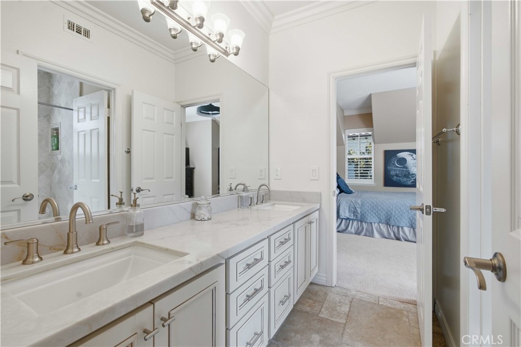 Bathroom with a long marble double-sink vanity and an adjoining bedroom with blue bedding.