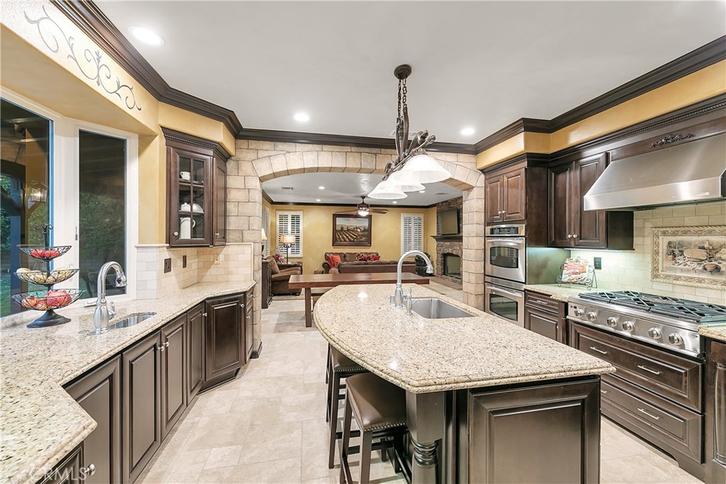 Kitchen with a curved granite island, dark wood cabinets, stainless steel appliances, and a stone archway.
