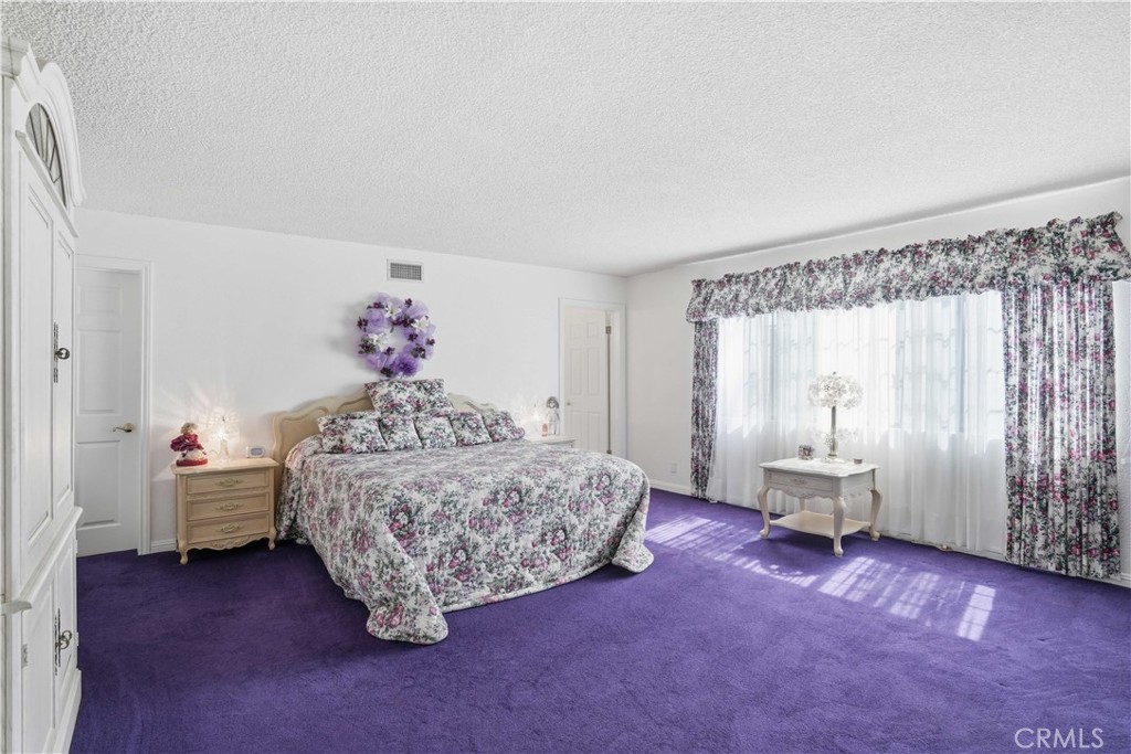 Bedroom with floral bedding, a bright window, and purple carpet.