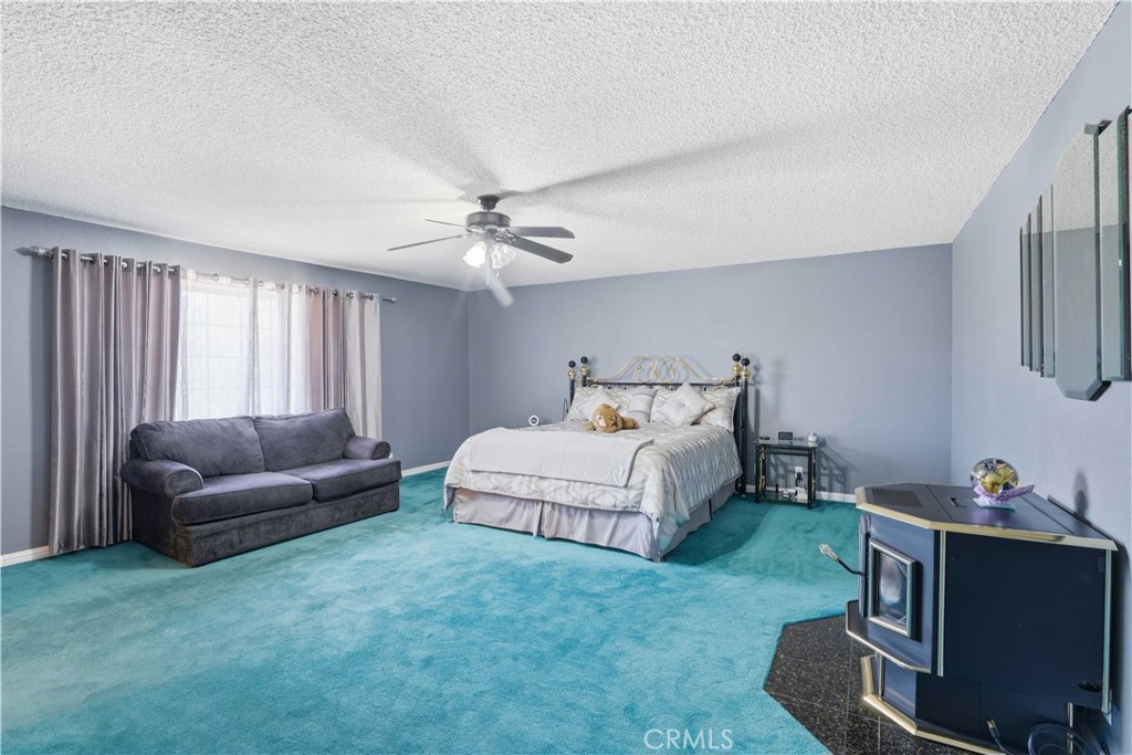 Bedroom with turquoise carpet, a white bed, and a dark sofa beneath a ceiling fan.