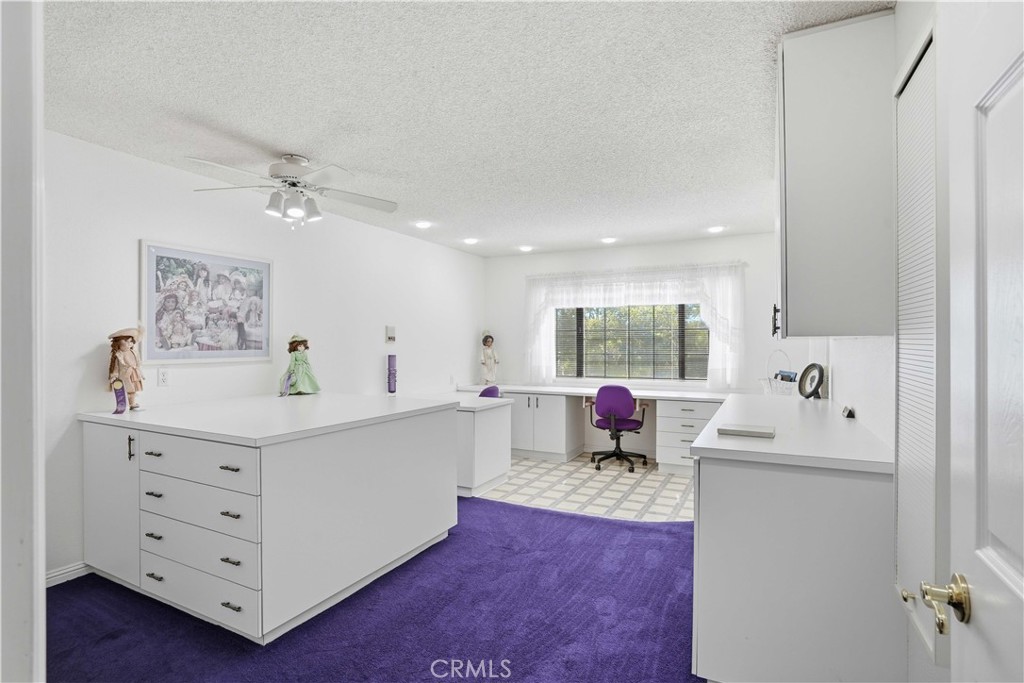 Home office with white built-in desks, purple carpet, and a window with blinds.