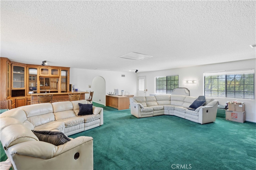 Living room with green carpet, white sectional sofas, a wooden built-in cabinet, and wide windows.