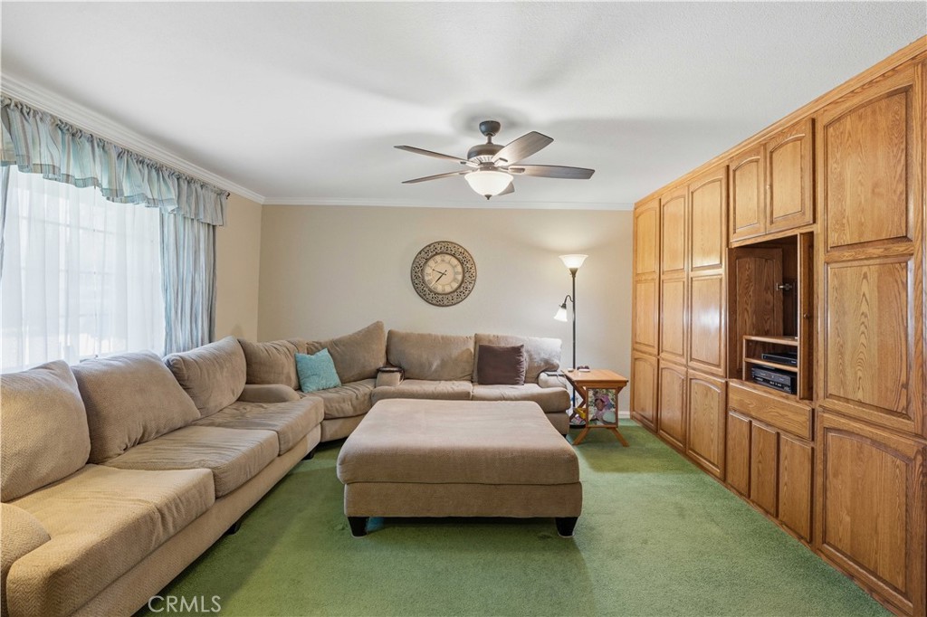 Living room with a beige sectional and ottoman, green carpet, and built-in wood cabinetry.