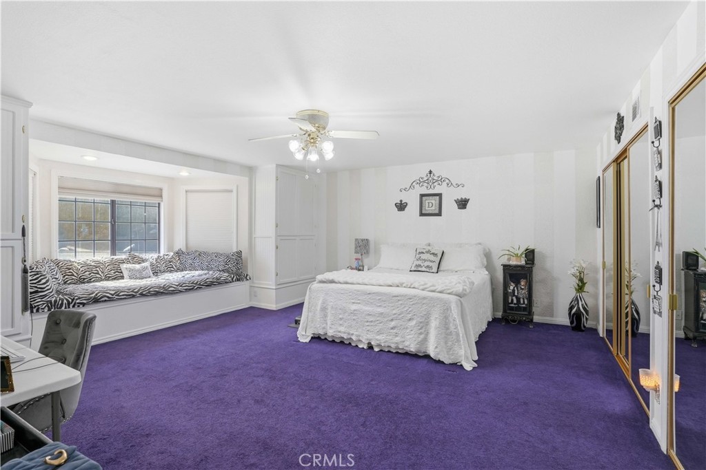 Bedroom with a white bed, purple carpet, zebra-patterned window seat, and mirrored closet doors.