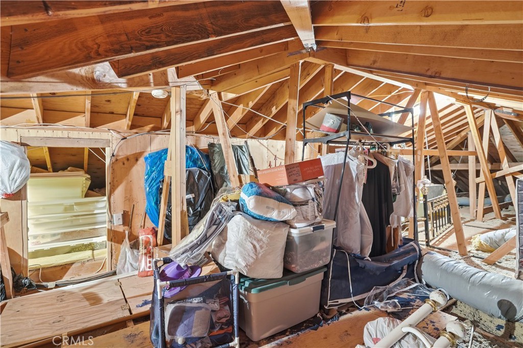Attic storage area with exposed wooden rafters and belongings stacked beneath the roof.