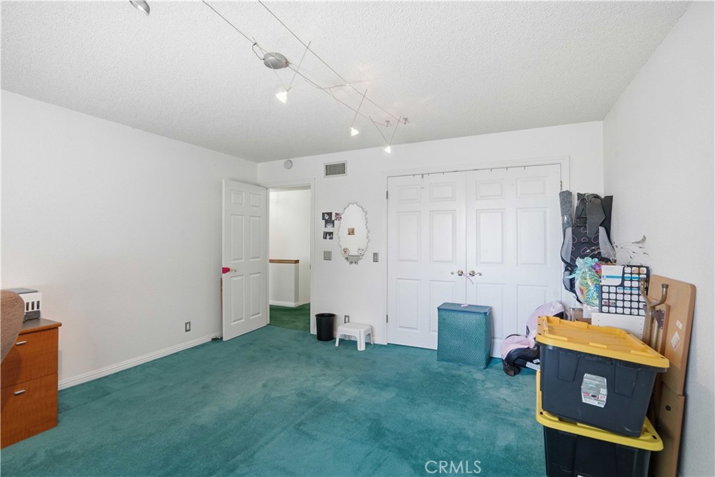 Bedroom with teal carpeting, white double closet doors, and storage bins.